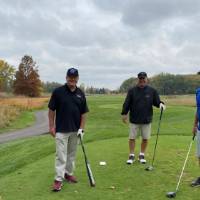 Four alumni on golf course with baseball bat